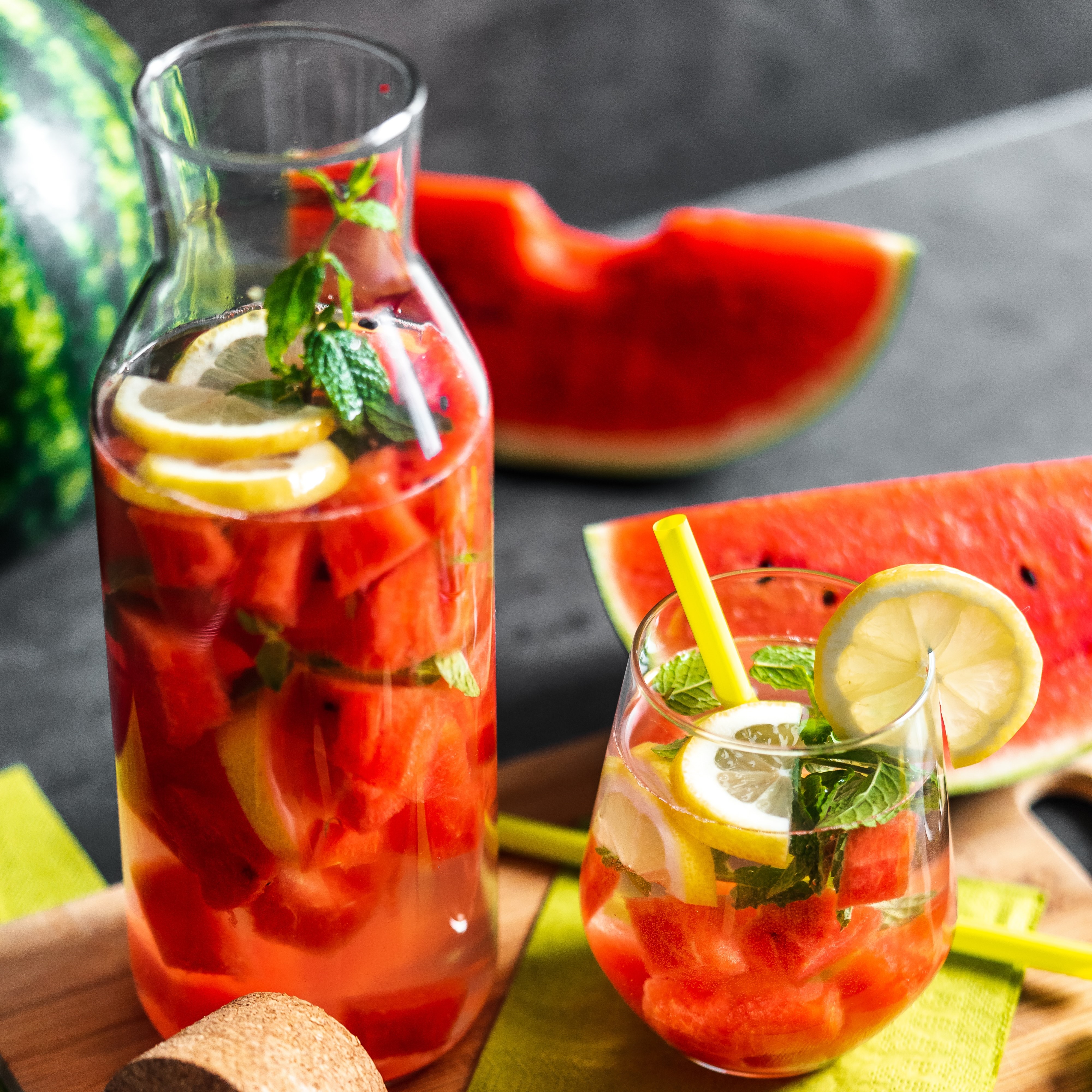 jug and glass filled with watermelon juice, lemon garnish. Large watermelon slice in the background.